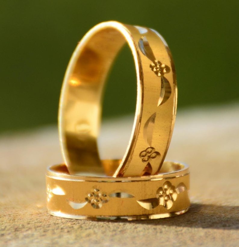 Close-up of two decorative gold wedding rings casting shadows on a warm surface.